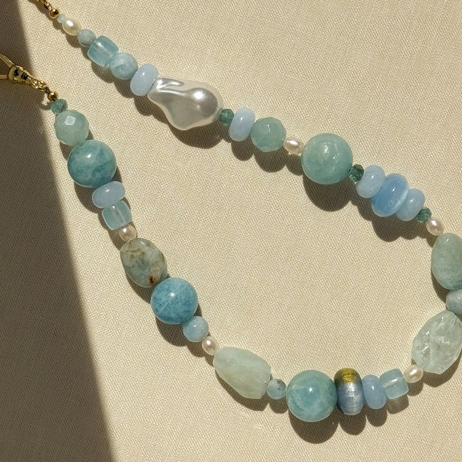 A beaded phone wristlet featuring light blue and white marbled beads and pearls with a gold clasp