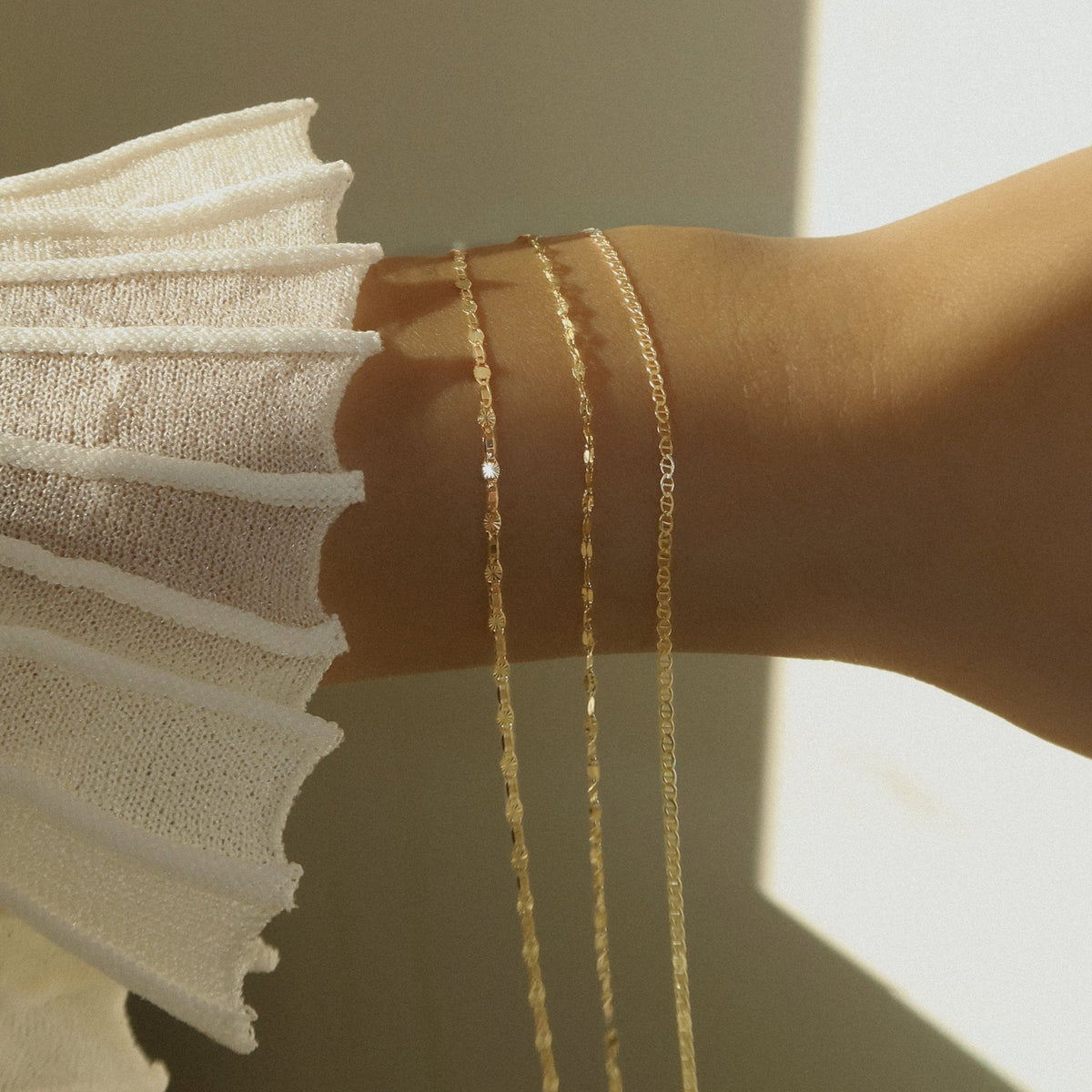 Three gold chains draped over a wrist as someone makes their chain selection.