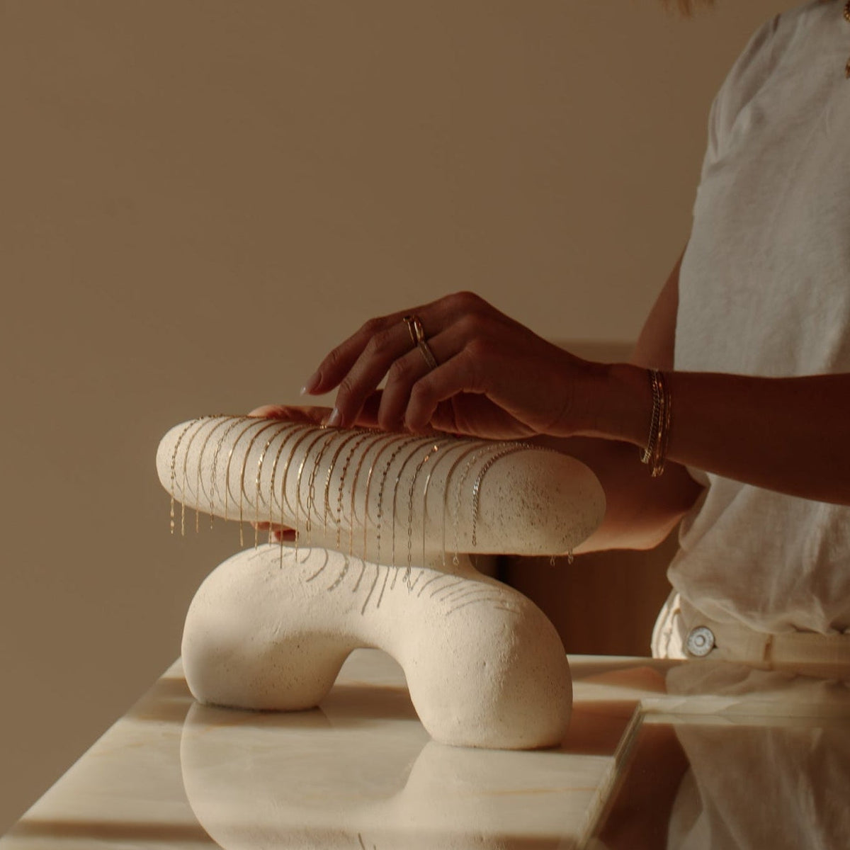 A woman in a white top reaches towards a selection of gold chains to be welded onto her wrist as a bracelet.
