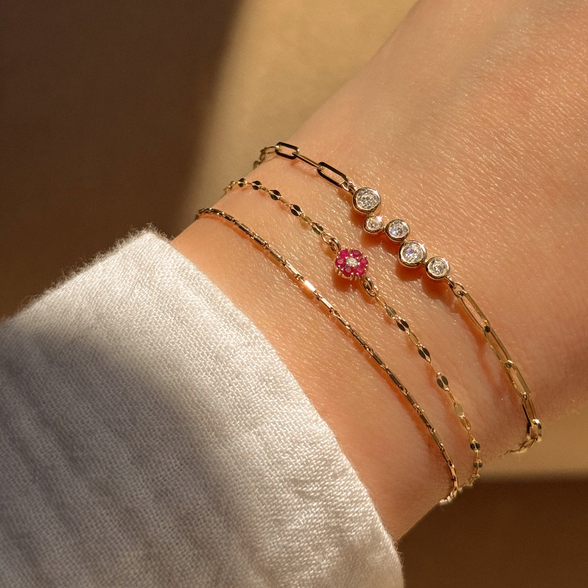 A close up of a wrist wearing three welded bracelets in gold with various charms